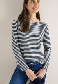 Haut à manches longues à rayures bleu marine et blanc, texture côtelée, avec un col bateau et de discrètes fentes latérales, associé à un jean en denim bleu.