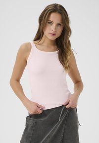 Débardeur rose clair à côtes avec un col arrondi, doté de larges bretelles et d'une coupe ajustée, associé à une jupe grise.