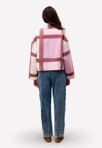 Roze en crèmekleurig geruit jasje met brede, contrasterende bordeauxrode strepen, oversized pasvorm en een kraag. Gecombineerd met losse spijkerbroeken en bruine schoenen.