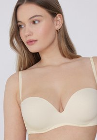 Krémová push-up podprsenka s hladkými, tvarovanými košíčky. Má nastavitelné ramínka a bezešvou konstrukci pro štíhlý vzhled.