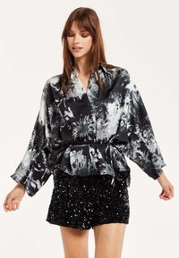 Black and white floral print blouse with a tied waist, long sleeves, and a relaxed fit, paired with black sequin shorts.