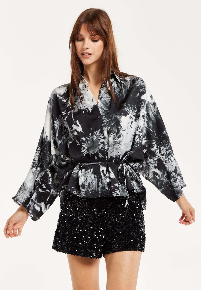 Black and white floral print blouse with a tied waist, long sleeves, and a relaxed fit, paired with black sequin shorts.