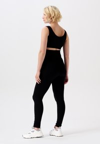 Schwarzes geripptes Crop-Top und hochgeschnittene Leggings, kombiniert mit weißen Sportschuhen, von hinten gesehen, betont die Textur des Stoffes.