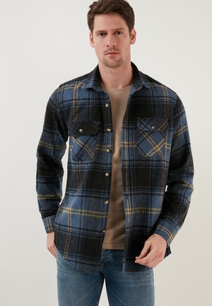 Flanel shirt in blauw en zwart ruitpatroon met gele accenten. Voorzien van een knoopsluiting aan de voorkant en twee borstzakken. Zacht, gestructureerd materiaal.