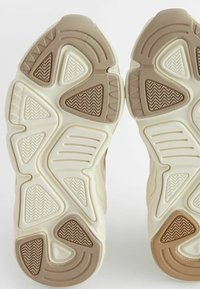 Semelles de chaussures de sport beige avec des motifs texturés. Comprend des rainures en zigzag et circulaires, des bords en caoutchouc prononcés et un design superposé.