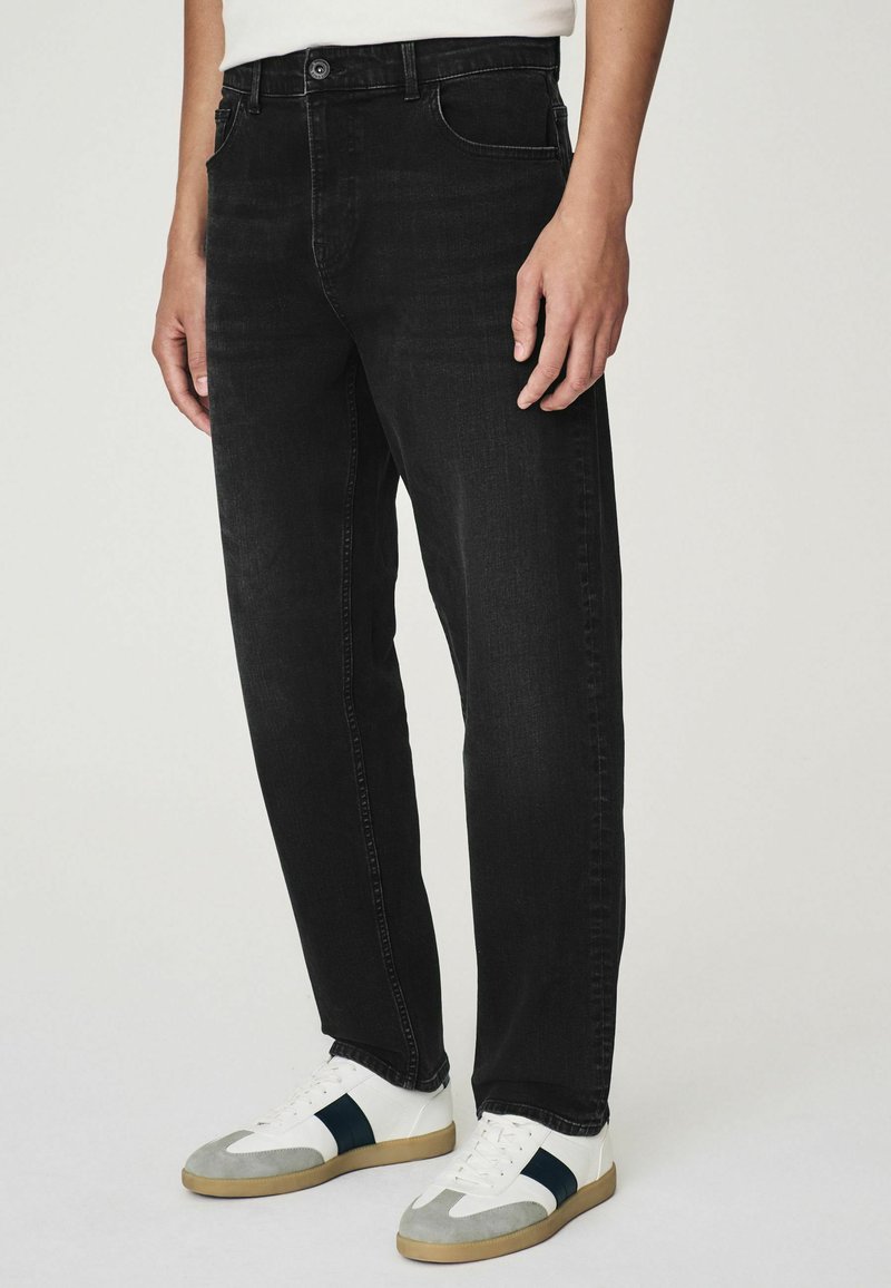 Svarta denimjeans med rak bendesign, femficksstil, subtil sömnad och klassisk knappstängning. Matchas med vita sneakers.