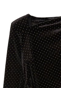 Haut en velours noir à manches longues, avec un motif à pois dorés. Encolure légèrement drapée et texture lisse. Étiquette de marque visible.