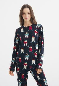 Dlouhý rukáv pyžamo v námořnické barvě se vzorem opakujících se dětí lyžujících, s červenými, bílými a modrými akcenty. Měkká, elastická tkanina.