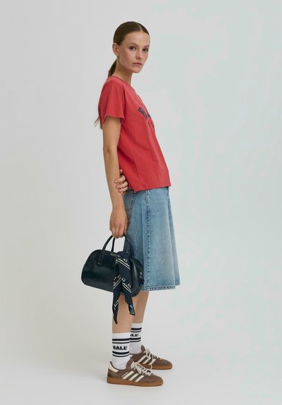 T-shirt en coton rouge avec motif, jupe midi en denim bleu, sac à main noir avec écharpe, chaussettes blanches avec rayures noires, baskets en daim marron.