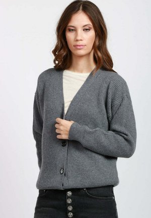 Cardigan grigio a coste con scollo a V, bottoni sul davanti e maniche lunghe. Indossato sopra una camicia chiara, caratterizzato da tessuto strutturato e vestibilità comoda.