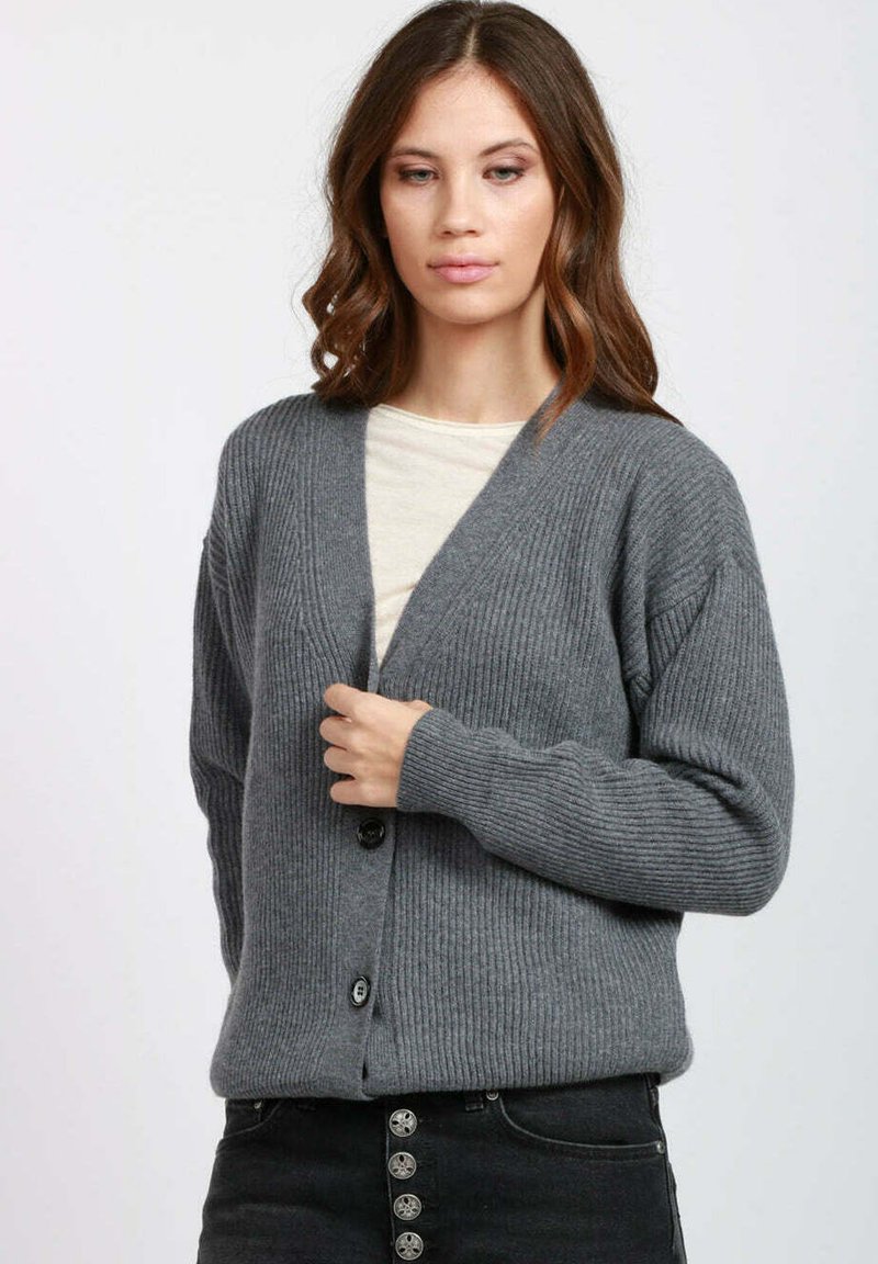 Cardigan grigio a coste con scollo a V, bottoni sul davanti e maniche lunghe. Indossato sopra una camicia chiara, caratterizzato da tessuto strutturato e vestibilità comoda.