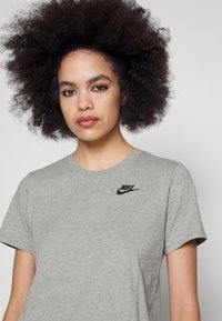 Pilkas medvilnės marškinėliai su apvalia iškirpte ir trumpomis rankovėmis, turintys mažą juodą Nike logotipą viršutinėje kairėje krūtinės dalyje.