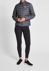 Grå pufferjacka med horisontella sömmar, ståkrage och logotyp. Svarta leggings och svarta sneakers fulländar outfiten.