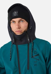 Giacca softshell teal con cappuccio nero e zip. Presenta un logo sul petto, accessori a contrasto e corde di regolazione sul cappuccio.