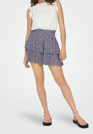 Jupe mini florale avec des volants en bleu, rose et vert, associée à un haut sans manches blanc. Tissu lisse avec une finition délicate en dentelle.