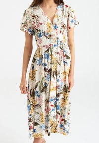 Blommig midiklänning med V-hals, korta fjäderlätt ärmar och figursydd midja. Har en krämfärgad bakgrund med blommönster i blått, gult och rött.