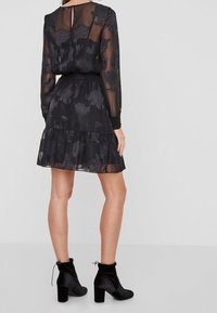 Svart genomskinlig klänning med blommönster, långa ärmar, smal midja och volangkant, tillsammans med svarta ankelskor.