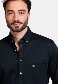 Donker marineblauw button-up shirt met een klassieke kraag, voorzak en logo-detail. Gemaakt van gladde stof met een gestructureerde pasvorm.