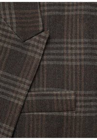 Tissu marron texturé avec un motif à petits carreaux gris et marron clair, montrant le revers d'une veste de costume et le détail d'une poche.