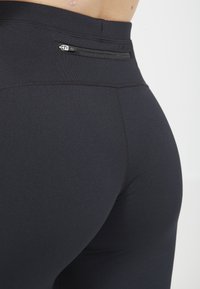 Svarta högmidjade leggings med en dragkedjeficka bak, tillverkade av ett glatt, elastiskt tyg med en figurnära design.