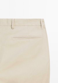 Beige pants back view showing belt loops and a single welt pocket with stitching detail.