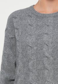 Sivkasta pletena pulover s teksturiranim kablom, okroglo izrezano obliko in dolgimi rokavi, narejen iz mehkega, tkanega materiala.