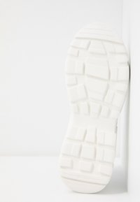 Semelle de sneaker blanche avec une surface texturée et à motifs, dotée de profondes rainures et de crampons carrés pour une meilleure adhérence. Design minimaliste avec des bords lisses.