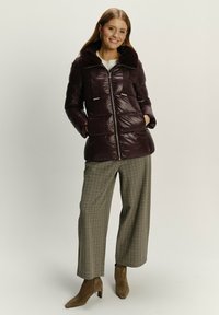 Burgunderfarbene Pufferjacke mit falschem pelzkragen, mit einem Reißverschluss vorne, aufgesetzten Taschen und schwarzen Bandakzenten, kombiniert mit karierten, weiten Hosen.