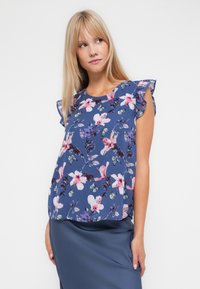 Blommig kortärmad topp med volangdetaljer, som har en blå bakgrund, rosa och lila blommor samt gröna fjärils mönster. Tillverkad av bomullsblandning.