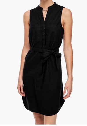 Ärmelloses schwarzes knielanges Kleid mit Knöpfen vorne, Brusttaschen und einem gebundenen Taillengürtel, getragen von einer stehenden Person.