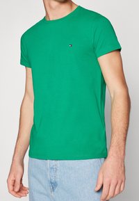 Zielona koszulka z krótkim rękawem wykonana z bawełny, z okrągłym dekoltem i małym logo na piersi. Gładka faktura i dopasowany krój.