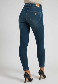 Smala mörkblå jeans med hög midja, denimtextur, läderlogotyp på baksidan och sidostygn, tillsammans med svarta högklackade skor.