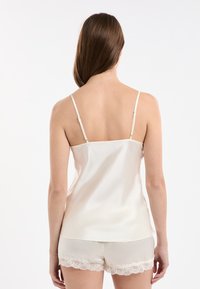 Satynowy top na ramiączkach w jasnym odcieniu kości słoniowej, w zestawie z dopasowanymi szortami z koronkowym wykończeniem na dolnej krawędzi. Gładka struktura materiału.