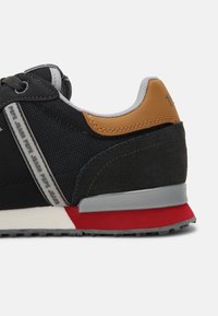 Baskets noires avec tige en mesh, accents en daim et talon en cuir marron. Semelle intermédiaire grise avec détails rouges ; branding sur le côté.