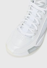 White athletic shoe with mesh and synthetic leather upper, featuring rounded toe, lace closure, and a visible air cushioning sole.