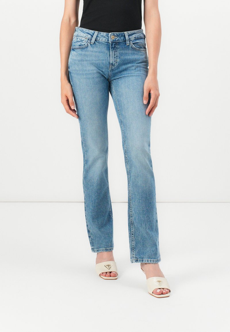 Light blue denim jeans with a straight leg design, featuring front pockets and a button closure. Worn with beige sandals.