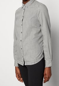 Grå denim skjorte med lange ærmer, knap-ned krave, frontknapper, lige kant og manchetter. Har en subtil tekstur og let glans.