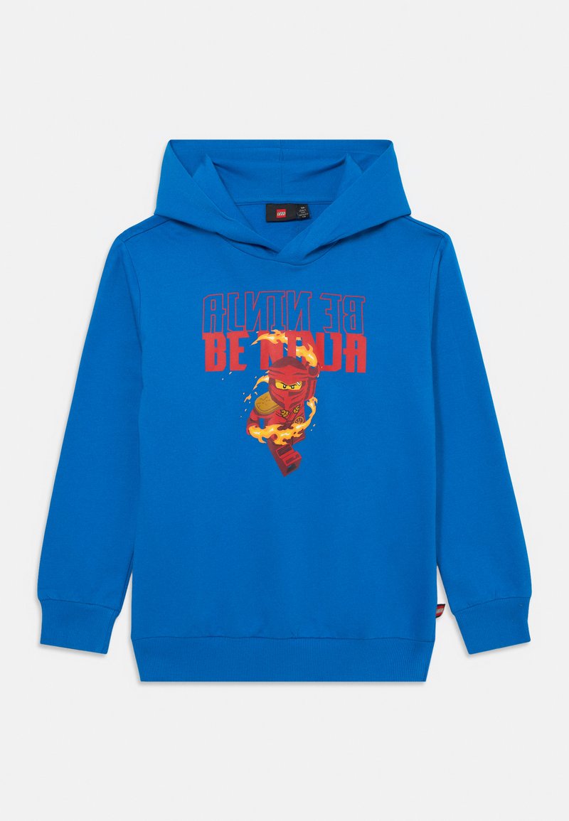 Zila kapuce, izgatavota no mīksta auduma, ar grafiku, kurā attēlots ninjas darbībā, un tekstu "Esi NINJA" sarkanā un oranžā krāsā.