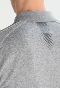 Gros plan sur le haut du dos d'une personne portant une chemise grise avec un col côtelé et un motif à pois sous le col.