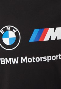 Logo BMW a M trojbarevné pruhy s částečným textem "BMW Motorsport" na černém textilním pozadí.