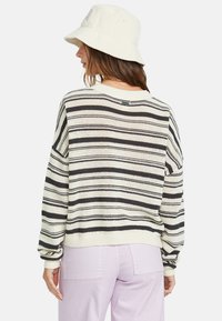 Striped knit sweater in cream and black, relaxed fit with ribbed cuffs and hem. Paired with pastel purple pants, featuring a bucket hat.