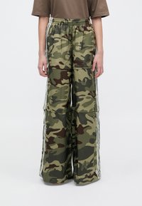 Zöld árnyalatú camo cargo nadrág széles, laza fitettel, rugalmas derékkal és fehér oldalsávokkal. Könnyű anyag, sima textúrával.