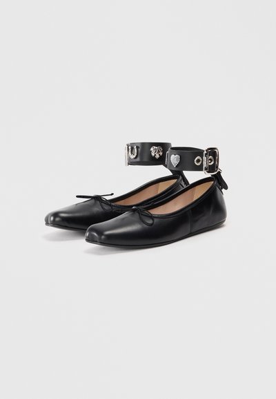 Black leather ballet flats with a pointed toe, featuring a decorative ankle strap with metallic accents and bow detail on the front.