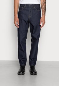 Donkerblauwe denim jeans met een rechte snit, oranje stiksels, vijf zakken en een knoopsluiting. Draag met zwarte enkellaarsjes.