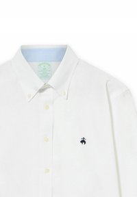 Bílá košile na knoflíky vyrobená z bavlny, se slim fit střihem, s světle modrým vnitřním límečkem a malým námořnickým logem na hrudi.