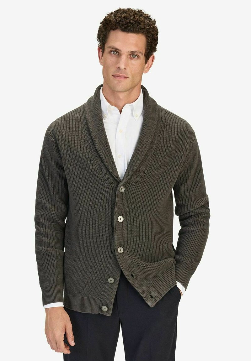 Mörkgrön ribbad cardigan med sjalkrage, knappar fram, och texturerad stickad mönster. Bärs över en vit skjorta med krage.