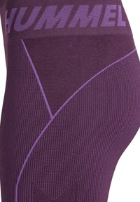 Zbliżenie fioletowych bezszwowych legginsów z prążkowaną teksturą, skośnymi liniami wzoru i logo "HUMMEL" na szerokim pasie.