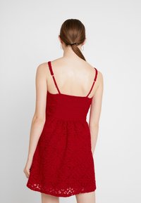 Rode kanten jurk met een aangesloten lijfje met geplooide details en een uitlopende rok. Dunne bandjes en een gekartelde zoom zorgen voor extra textuur.