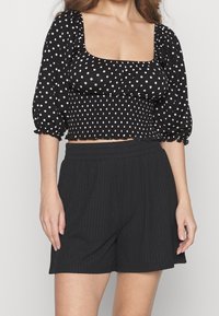 Černý crop top s puntíky, čtvercovým výstřihem a nařaseným korpusem; spárován s černými žebrovanými šortkami s elastickým pasem.