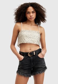Top in tessuto metallico tagliato con motivo a quadrati, abbinato a pantaloni corti in denim neri a vita alta con orlo sfrangiato e cintura dorata.